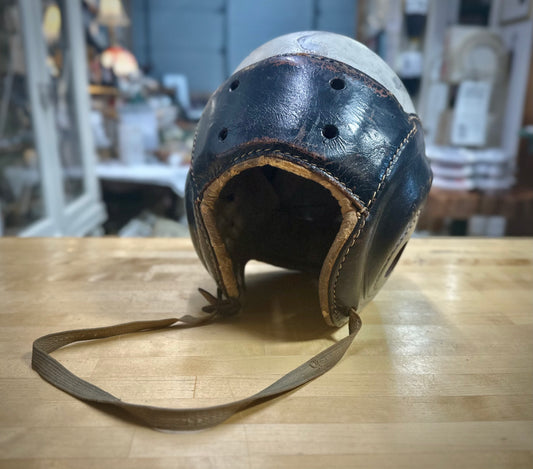Vintage leather helmet with a chin strap on a wooden surface