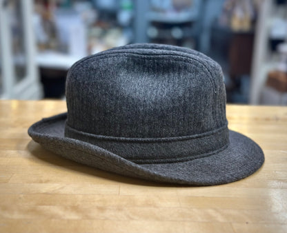 Gray fedora hat on a wooden surface with a blurred indoor background