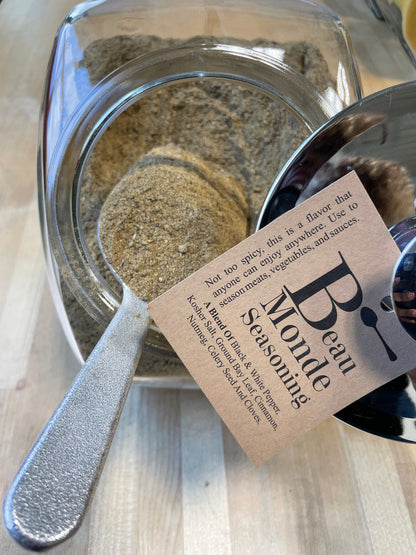 Beau Monde pepper, bay leaf and warm spice blend in a glass jar with a metal scoop