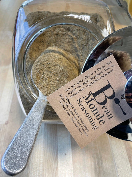Beau Monde pepper, bay leaf and warm spice blend in a glass jar with a metal scoop
