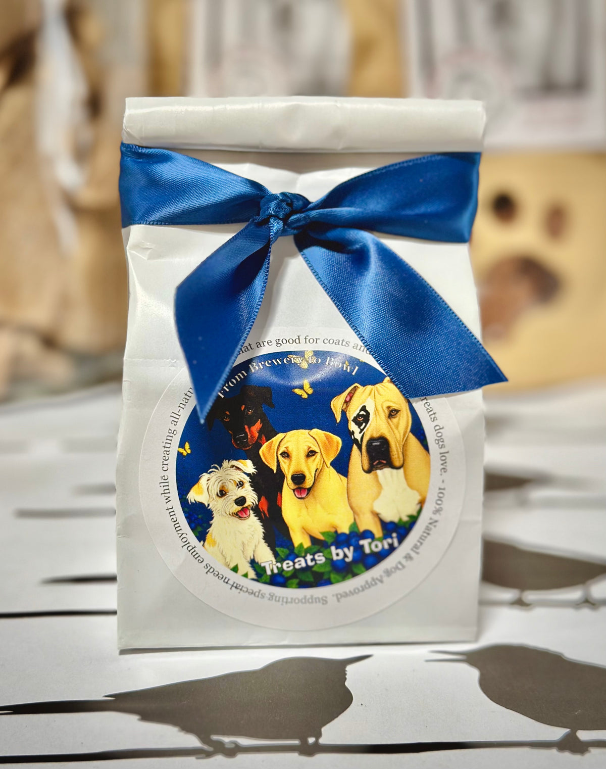 Treats by Tori blueberry dog treats in a white gift bag with blue ribbon
