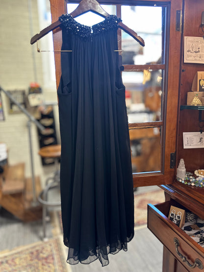 Full-length back view of the vintage black Saks Fifth Avenue evening gown, showing the flowing gathered chiffon silhouette, embellished shoulders and side details.