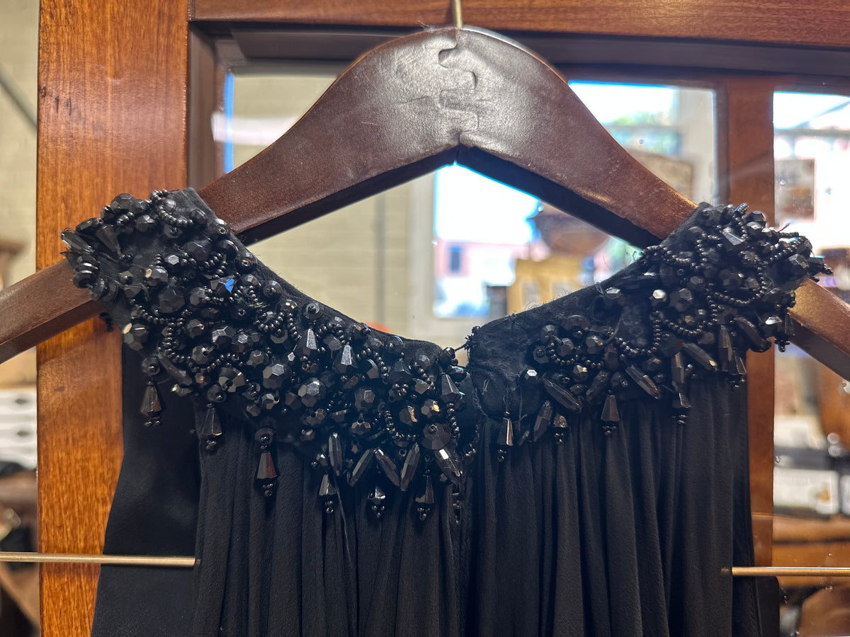 Close-up of the back neckline and shoulders featuring elaborate black-on-black beadwork with faceted beads, sequins, seed beads and elongated dangling accents with a few missing beads.