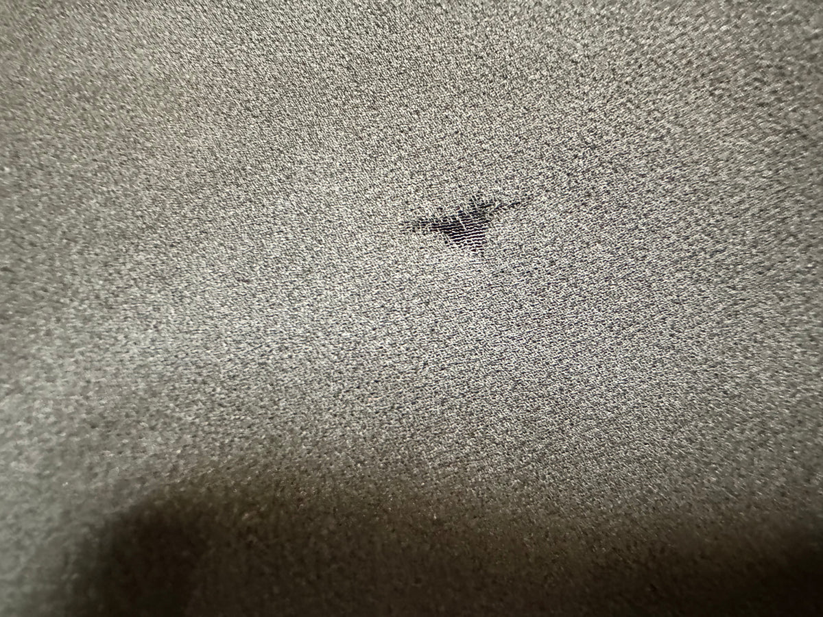 Close-up condition photo showing a small hole or tear in the sheer black fabric of the vintage evening gown.