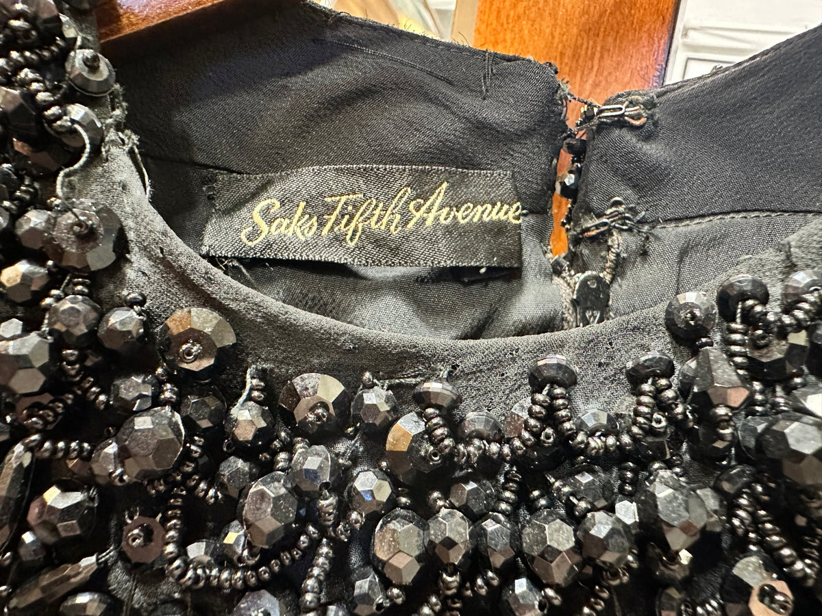 Close-up of the Saks Fifth Avenue label inside a vintage black evening gown, surrounded by intricate black faceted bead, seed bead and sequin embellishment.