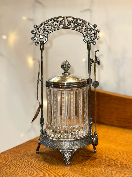 Vintage glass biscuit jar with ornate silver-tone metal stand, decorative arched handle, and fitted lid.