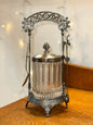 Vintage glass biscuit jar with ornate silver-tone metal stand, decorative arched handle, and fitted lid.