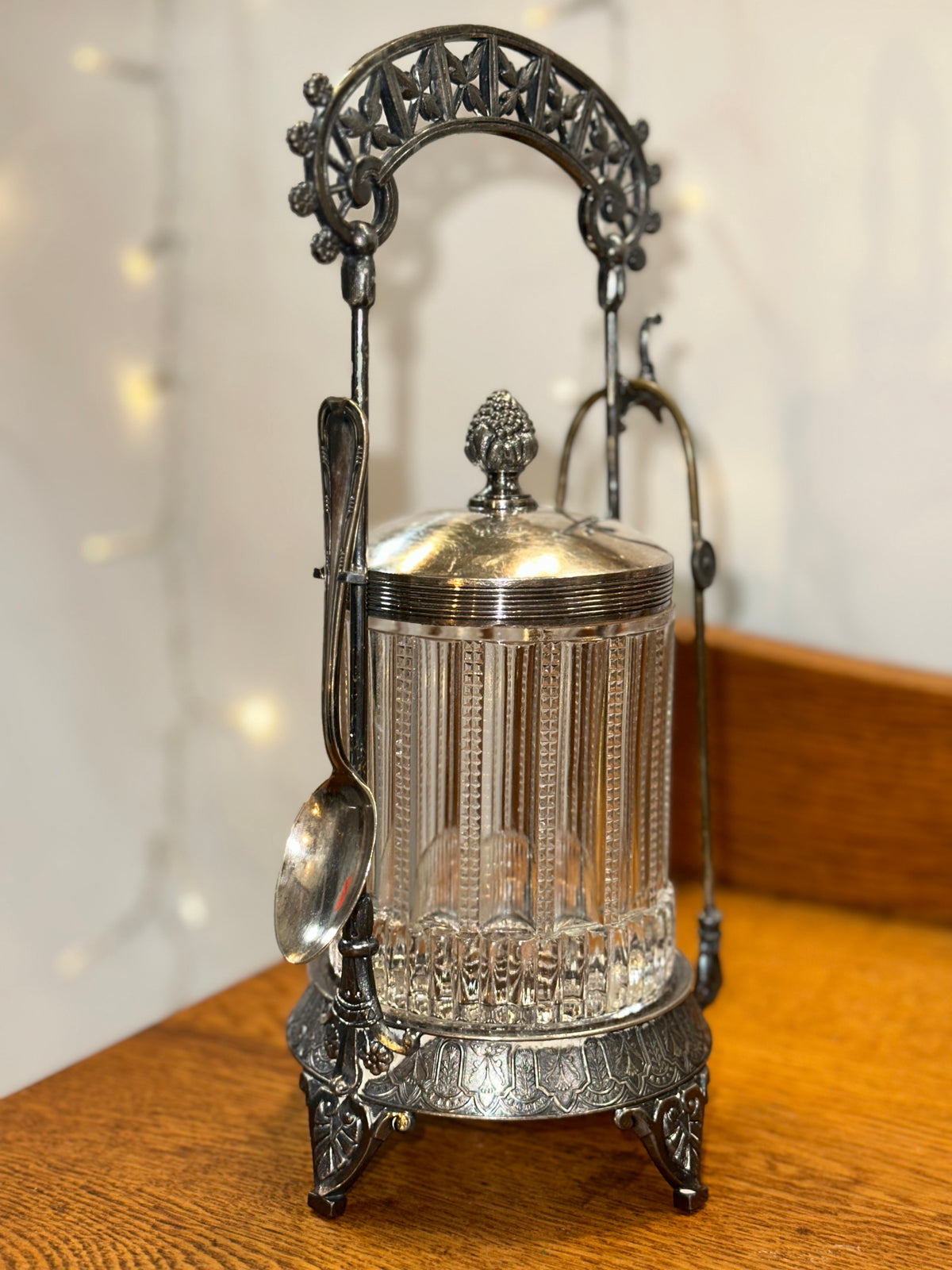Front view of a vintage ribbed glass biscuit jar with an ornate silver-plated stand and decorative metalwork.