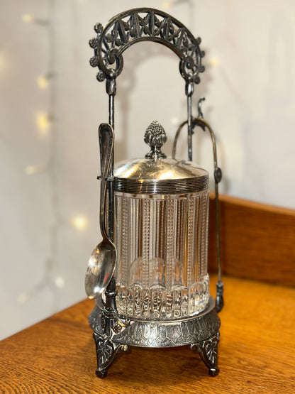 Front view of a vintage ribbed glass biscuit jar with an ornate silver-plated stand and decorative metalwork.