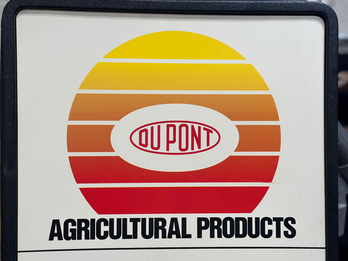 Close-up of the upper portion of the vintage clock showing the original yellow, orange, and red DuPont Agricultural Products advertising graphic and DuPont logo.