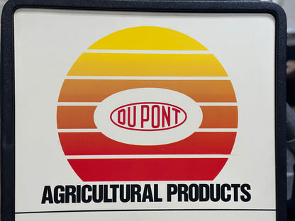 Close-up of the upper portion of the vintage clock showing the original yellow, orange, and red DuPont Agricultural Products advertising graphic and DuPont logo.
