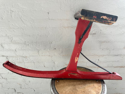 Side view of antique Pritchard jack jumper sled showing curved wooden runner, raised seat and original red paint.