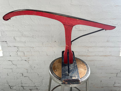 Antique jack jumper sled displayed upside down, showing the metal runner, original red paint, black seat and support bracing.