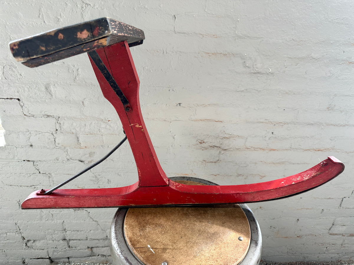 Side profile of antique New England jack jumper sled with red-painted wooden runner and raised black seat.