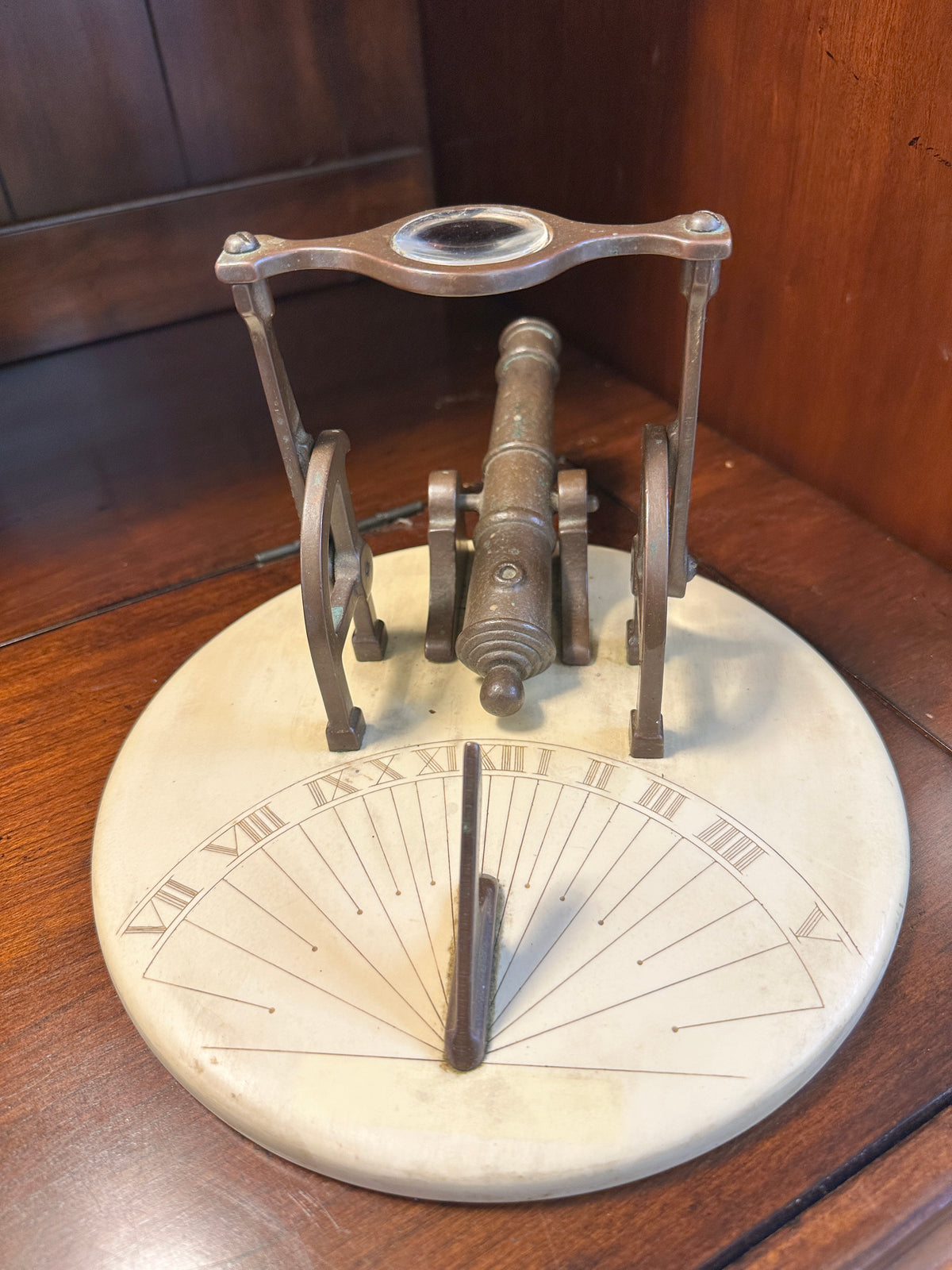 Vintage brass noon cannon sundial showing engraved Roman numeral hour markings, upright gnomon and magnifying lens assembly.