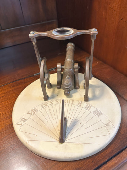 Vintage brass noon cannon sundial showing engraved Roman numeral hour markings, upright gnomon and magnifying lens assembly.