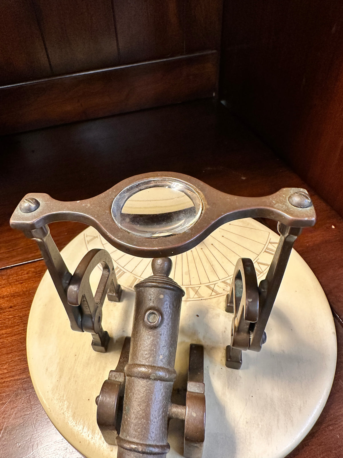 Overhead view of vintage noon cannon sundial highlighting brass cannon, curved lens supports and engraved Roman numeral markings.