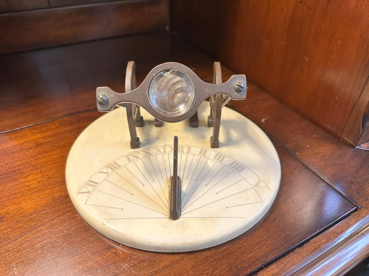 Top-down close-up of chipped glass magnifying lens mounted in ornate brass-toned frame above vintage cannon sundial.