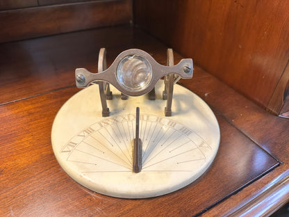 Top-down close-up of chipped glass magnifying lens mounted in ornate brass-toned frame above vintage cannon sundial.