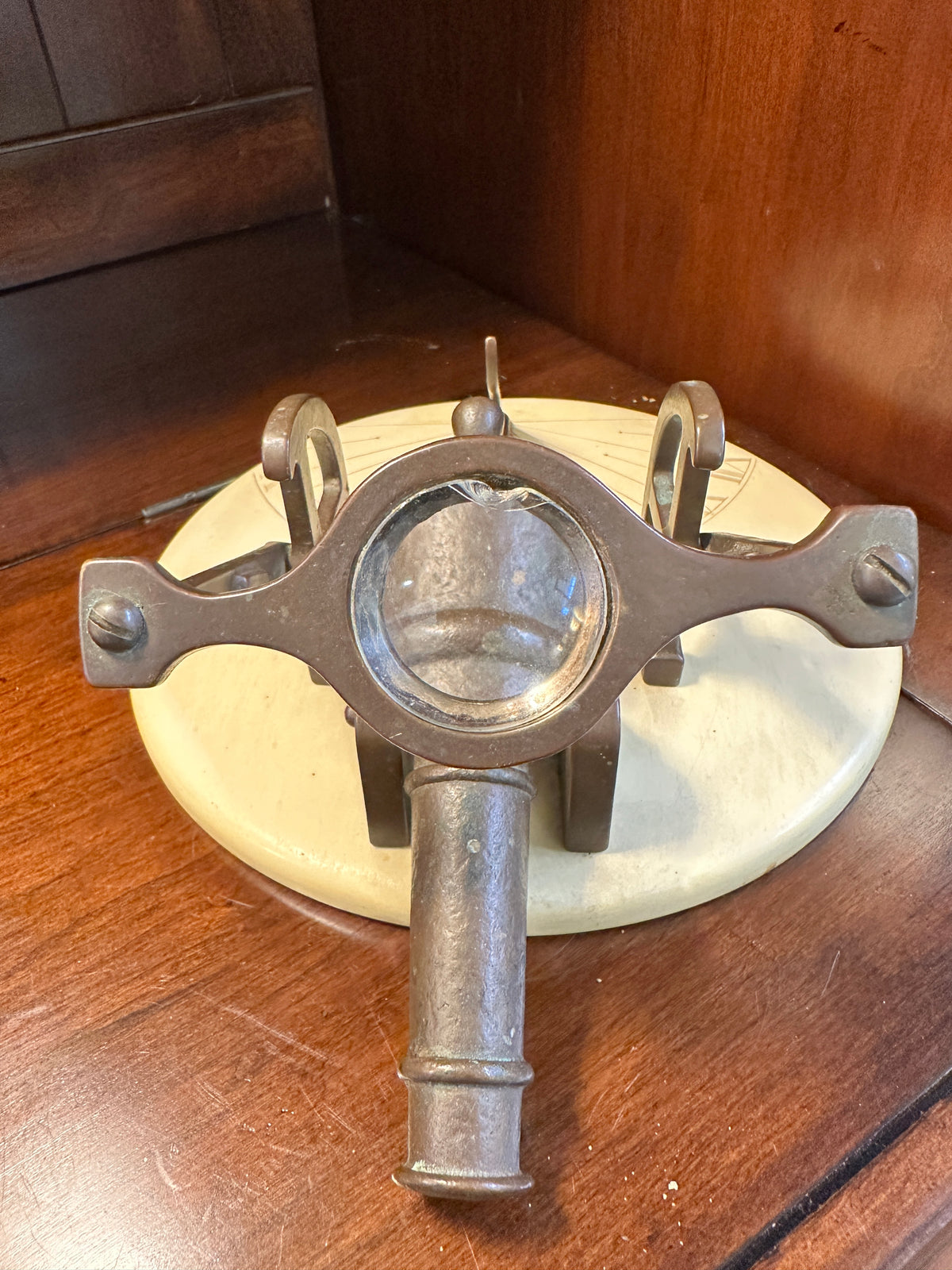 Close-up of vintage brass noon cannon sundial showing chipped magnifying glass, ornate metal supports and cream-colored circular base.