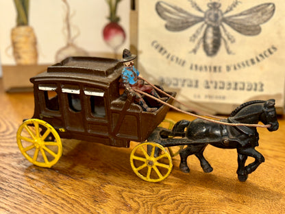 Vintage cast iron horse-drawn stagecoach with cowboy driver and yellow wheels